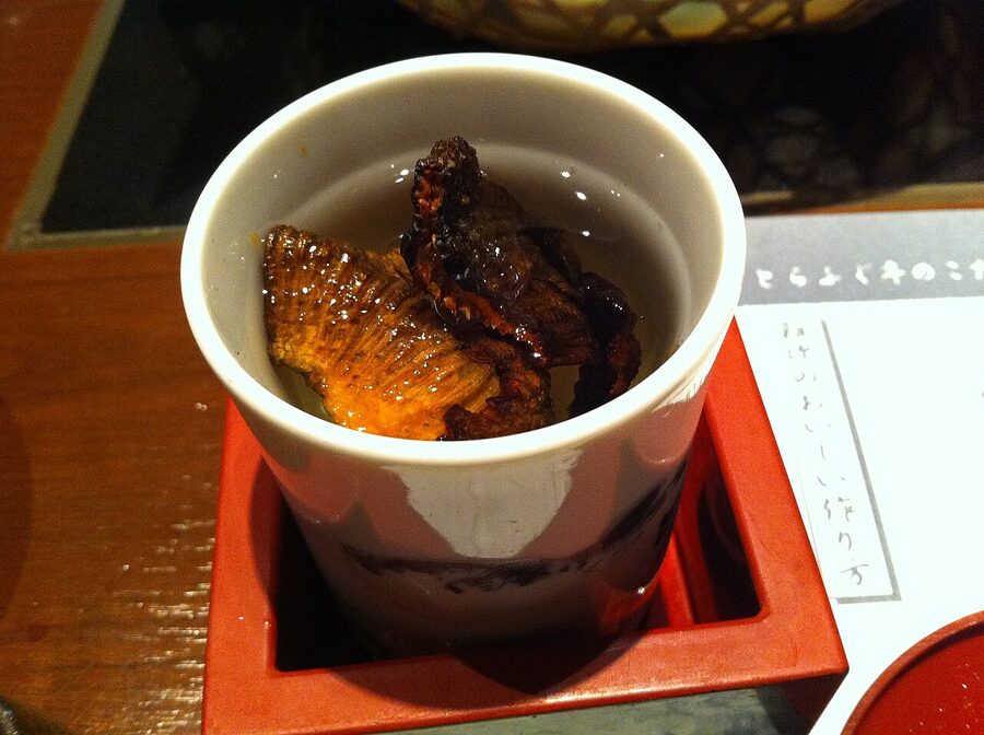 A close-up of hirezake at a Japanese counter, charred fugu fin afloat in scalding sake