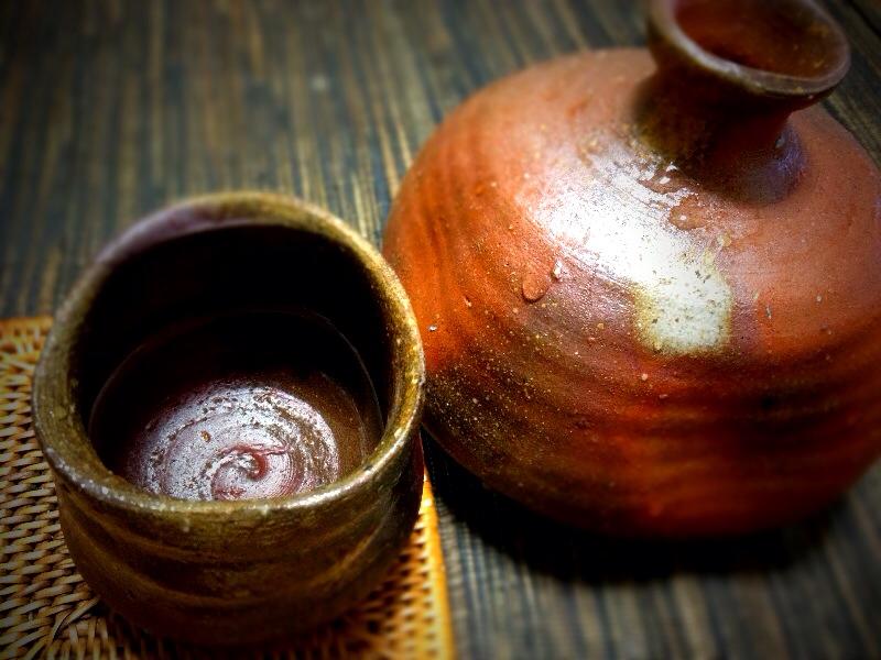 A black ceramic tokkuri sake decanter and matching sakazuki cup on a wooden Japanese counter