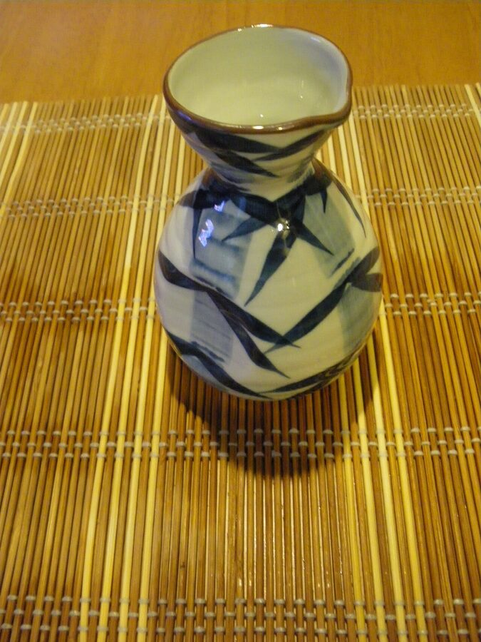 A small tokkuri of warmed sake on a wooden table next to traditional Japanese small dishes