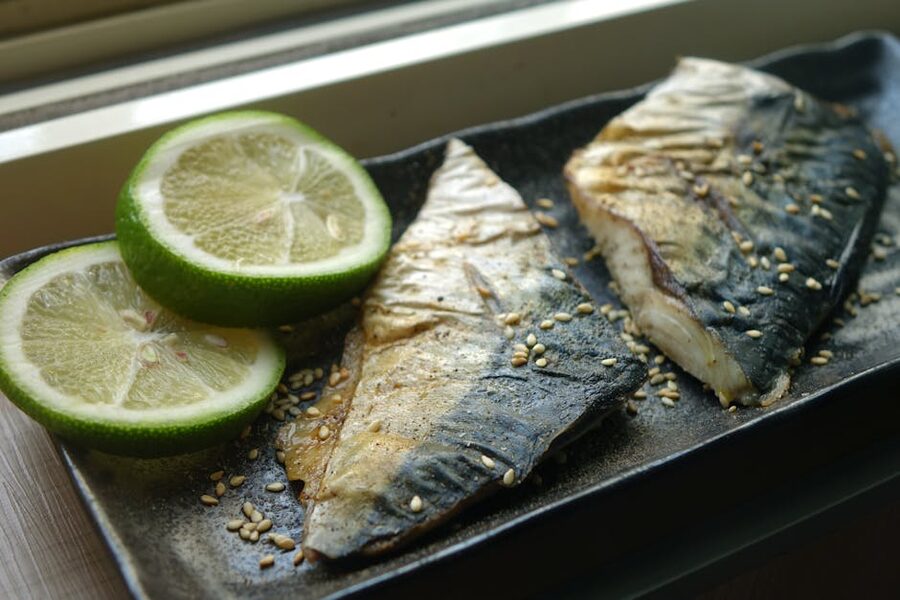 Plate of grilled mackerel served with lime slices and sesame seeds