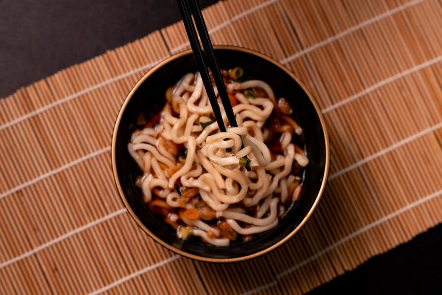 Bowl of thick udon noodles with chopsticks against a dark surface