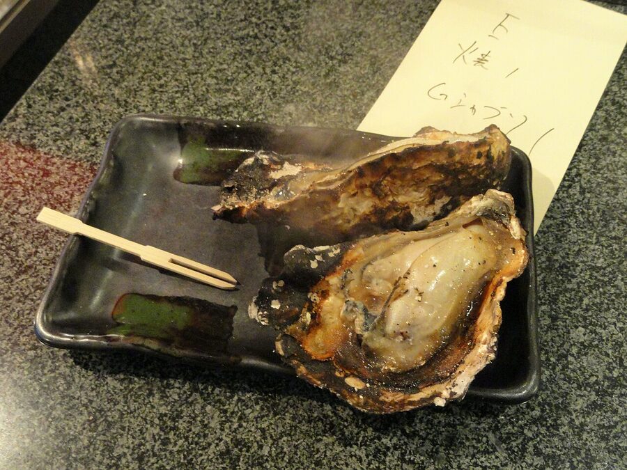 Grilled oysters yakigaki cooking on a metal grate at a Miyajima stall