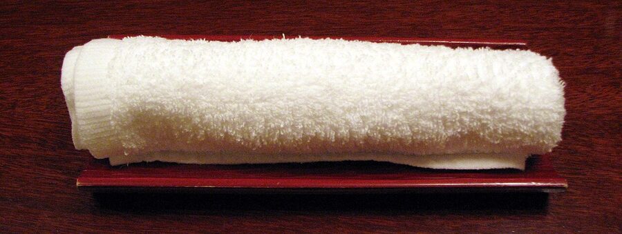 A rolled hot oshibori towel on a small ceramic dish at a Japanese izakaya
