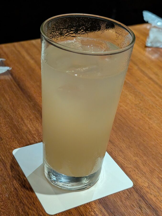 A small ceramic dish with appetiser sitting beside a glass of pear liqueur on the counter at an Ebisu izakaya