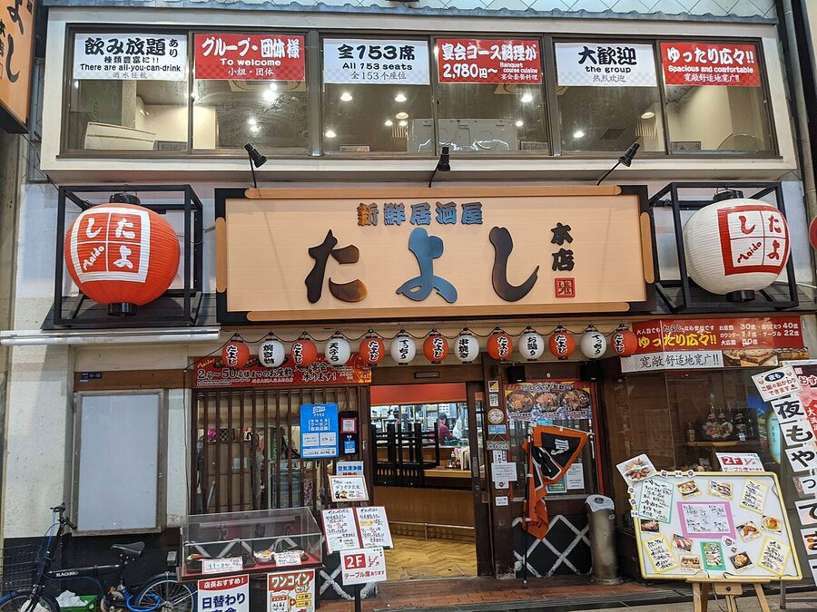 The lit-up exterior of Tayoshi izakaya in Sennichimae, Osaka at night with red lanterns