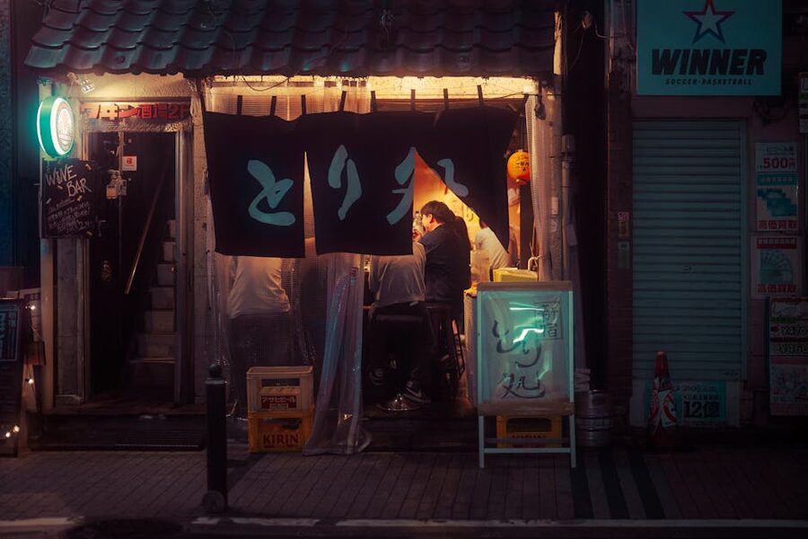 A warm Tokyo izakaya at night with red lanterns and a wooden interior visible through the open door