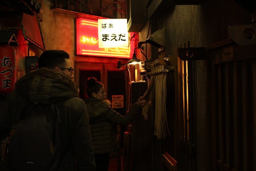 A narrow Tokyo izakaya alley at night with people entering, lit by neon signs