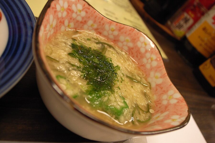 A small ceramic bowl of otoshi appetizer on a wooden table at a Japanese izakaya