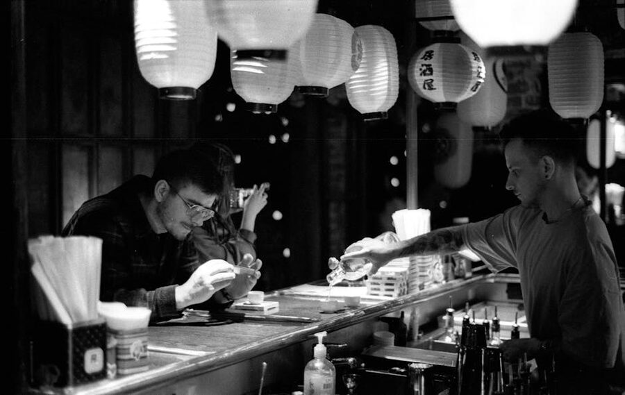 Atmospheric black and white photo of a bartender serving spirits under low light