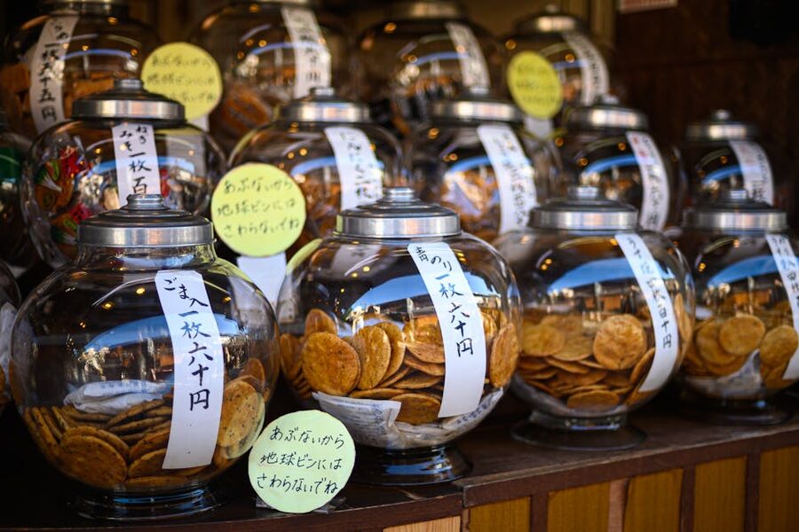 Rows of senbei rice crackers in glass jars on shop shelves