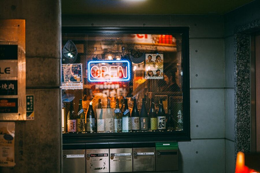 Sake bottles in a Japanese shop window with neon sign reflecting