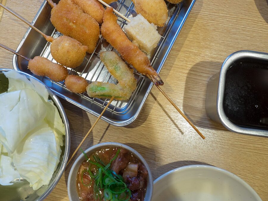 Kushikatsu skewers on a counter in Shinsekai, Osaka, beside a beer mug