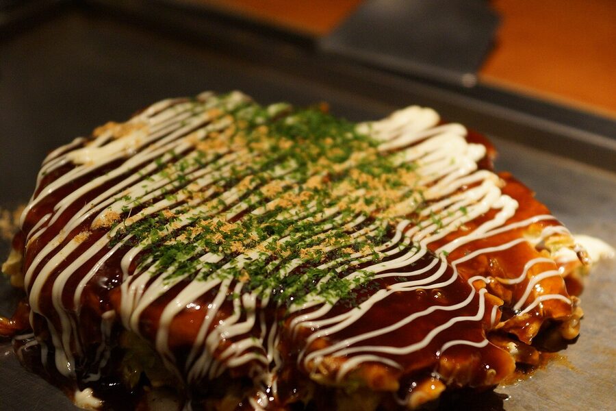 Okonomiyaki on the griddle in an Osaka restaurant with sauce being painted on