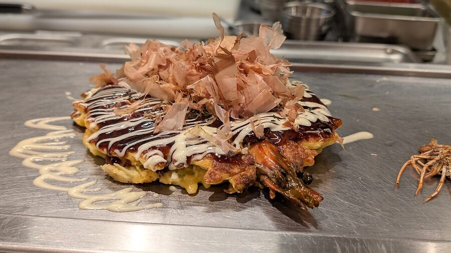 A finished okonomiyaki on a teppan grill in Osaka with bonito flakes