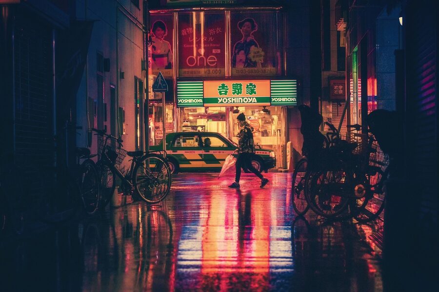 A neon-lit alley in Osaka at night with vending machines and small bars