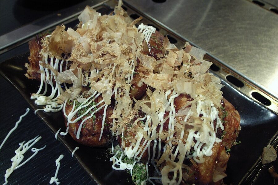 Takoyaki cooking on a hot griddle, octopus pieces visible in the batter