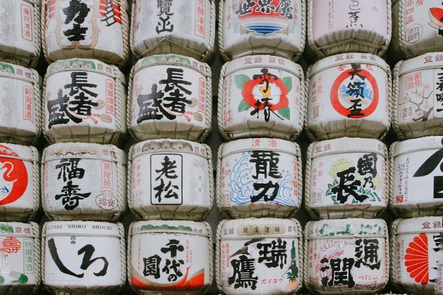 A stacked display of traditional Japanese sake barrels with brewery calligraphy on each cask