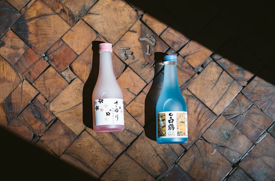 Two sake bottles in pink and blue casting shadows on a wooden surface