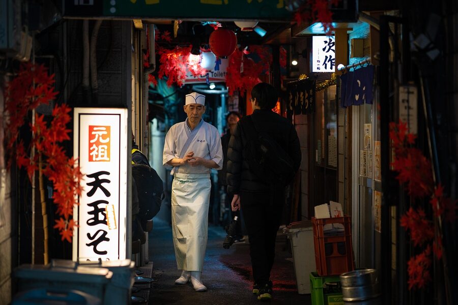 Cook walking through Omoide Yokocho carrying supplies
