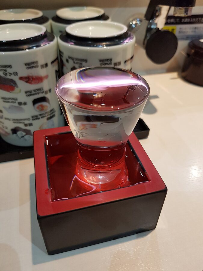 Sake glass overflowing into a wooden masu cup at a sushi restaurant in Asakusa