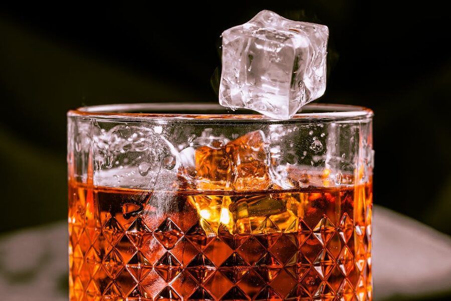 Whisky in a cut glass with a hand-cut ice ball mid-pour