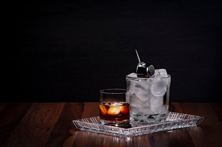 Whisky glass with ice cubes on a wooden bar surface