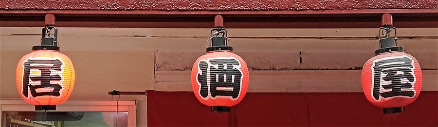 Red paper lanterns hanging outside an izakaya, marking a drinking street at night