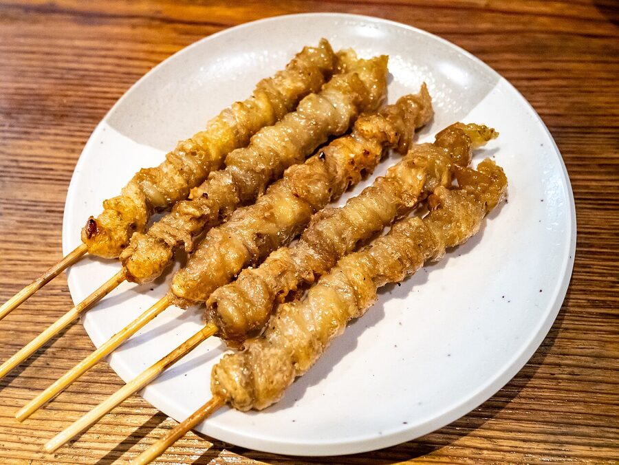 A row of Hakata-style chicken-skin skewers (torikawa) cooked dark and crisp