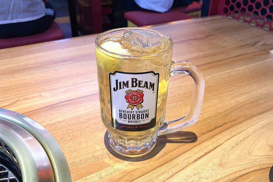 A highball glass on a counter, ice cold, the bourbon-style golden colour