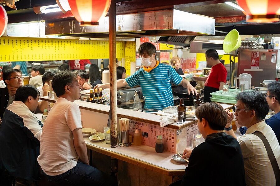A close-up of a packed Omoide Yokocho yakitori counter with diners and the cook visible through the smoke