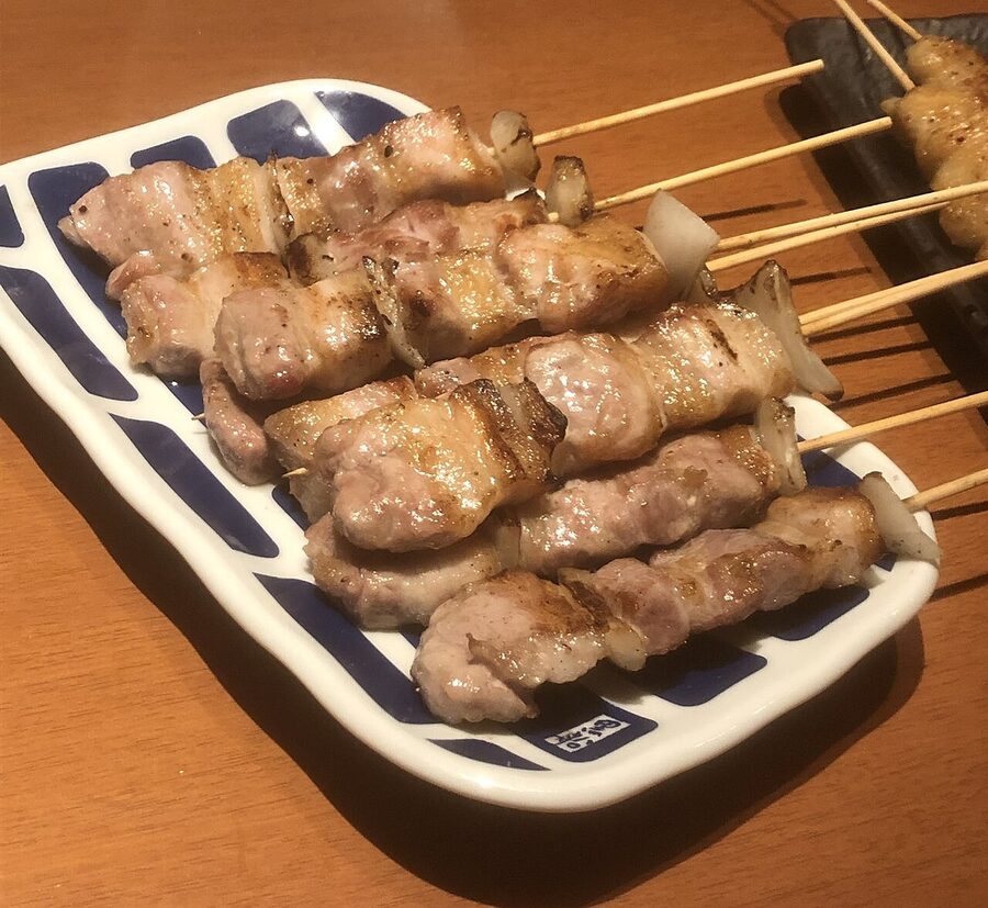 A row of Kyushu-style pork belly skewers, dark with the tare glaze, ready to leave the grill
